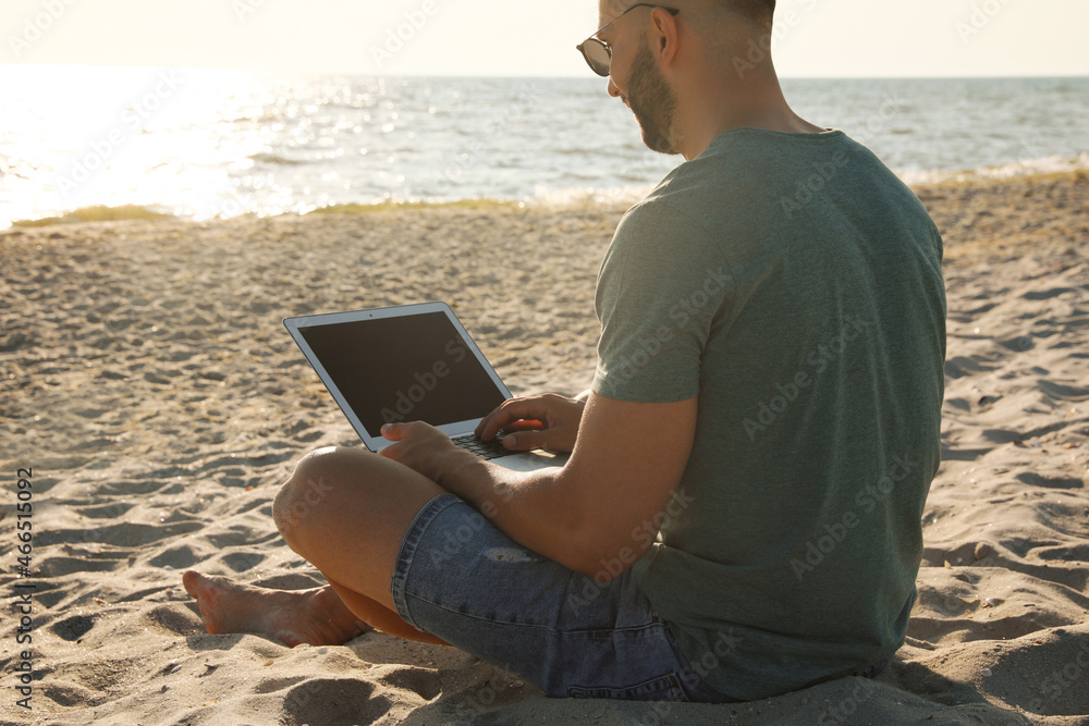 Man working with modern laptop on beach, closeup