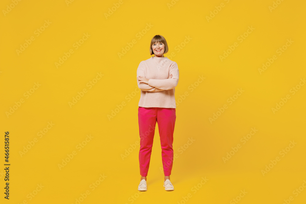 Full body elderly smiling happy woman 50s with bob haircut wears pink casual knitted sweater hold hands crossed folded isolated on plain yellow background studio portrait. People lifestyle concept Full body elderly smiling happy woman 50s with bob haircut wears pink casual knitted sweater hold hands crossed folded isolated on plain yellow background studio portrait. People lifestyle concept
