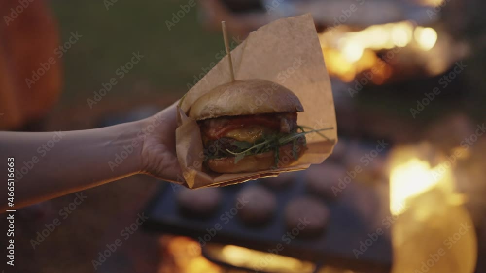 Hands holding beef burger with fire in the background Hands holding beef burger with fire in the background