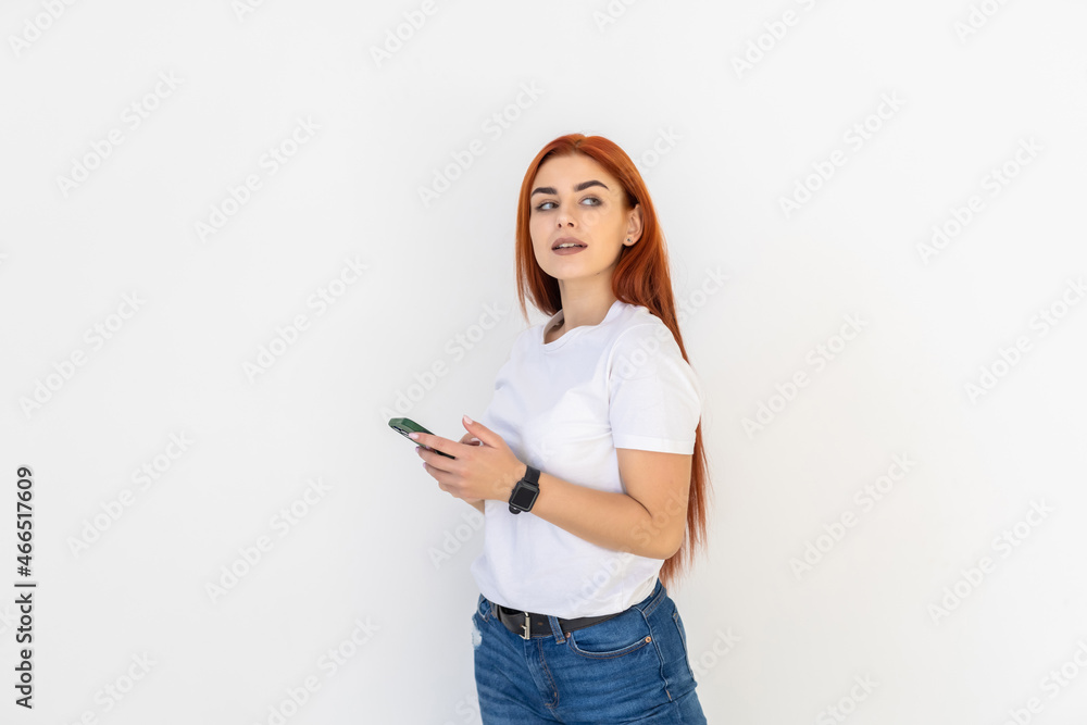 Portrait of a smiling redhead woman holding phone and texting over white background