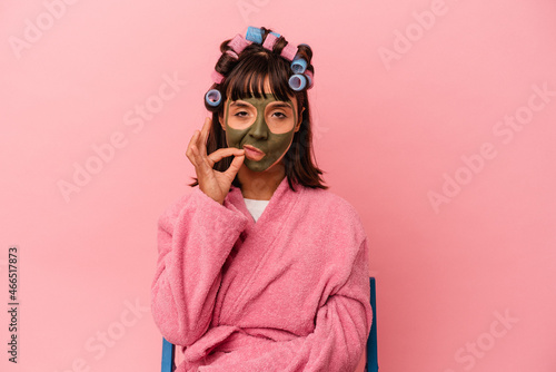 Young mixed race woman getting pretty in a house isolated on pink background with fingers on lips keeping a secret. © Asier