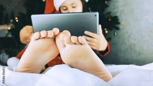 Feet close up. A child in a Santa hat plays on a tablet or communicates with his grandparents. Concept of christmas and new year