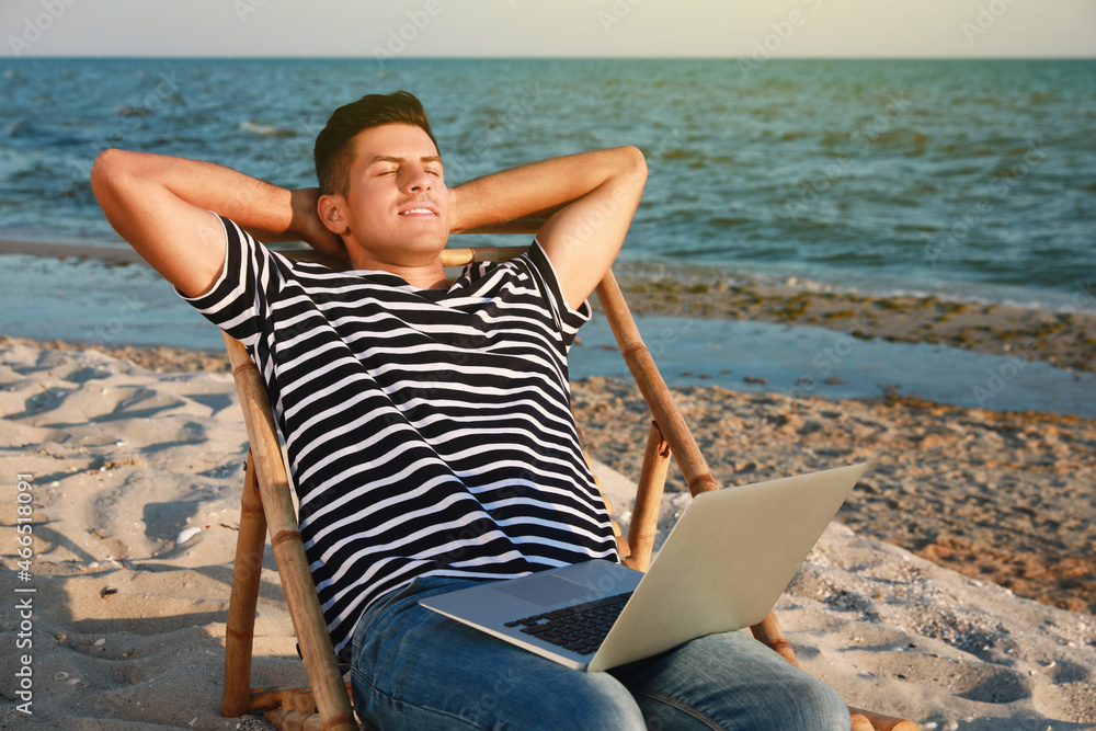 Man with laptop relaxing in deck chair on beach