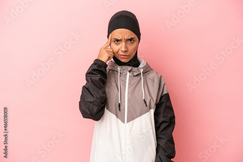 Young Arab woman with sport burqa isolated on pink background pointing temple with finger, thinking, focused on a task.