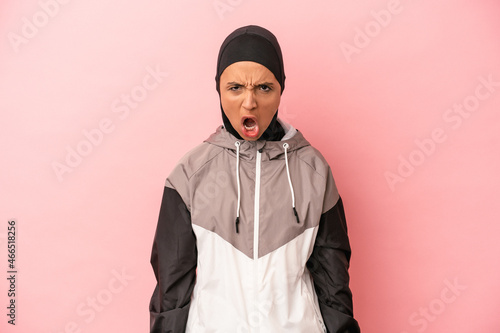 Young Arab woman with sport burqa isolated on pink background screaming very angry and aggressive.