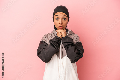 Young Arab woman with sport burqa isolated on pink background praying for luck, amazed and opening mouth looking to front.