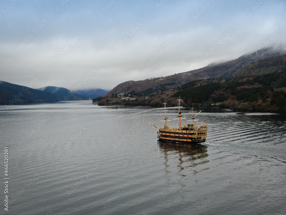 A semi-antique wooden tourist ship sails against the backdrop of a Japanese landscape