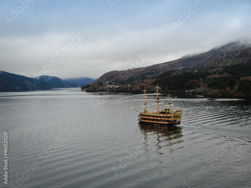 A semi-antique wooden tourist ship sails against the backdrop of a Japanese landscape