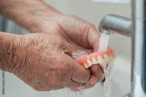 Asian senior or elderly old woman patient holding and washing denture in nursing hospital ward; healthy strong medical concept