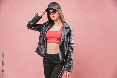 nice looking attractive girl in sunglasses in black cap posing while standing on pink background