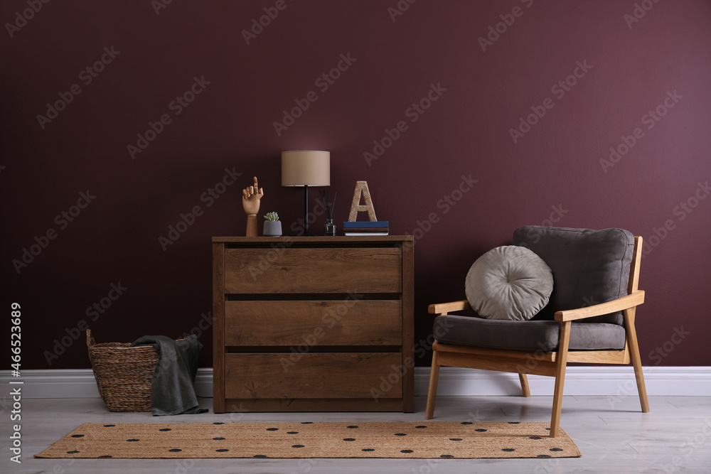 Fototapeta premium Elegant room interior with stylish chest of drawers and comfortable armchair near brown wall