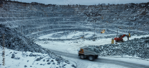 Panorama of a limestone quarry, with an unsharp mining truck moving in the foreground, in winter during night work.