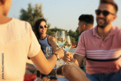 Group of friends having picnic outdoors at sunset, focus on glasses