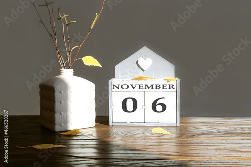 Calendar for November 6: name of the month in English, numbers 0 and 6 birch branch with one yellow leaf, fallen birch leaves on a wooden table, gray background, rays of the sun photo