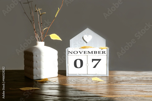 Calendar for November 7: name of the month in English, numbers 0 and 7 birch branch with one yellow leaf, fallen birch leaves on a wooden table, gray background, rays of the sun photo