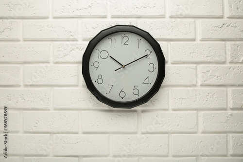 Black wall clock on the white wall background.