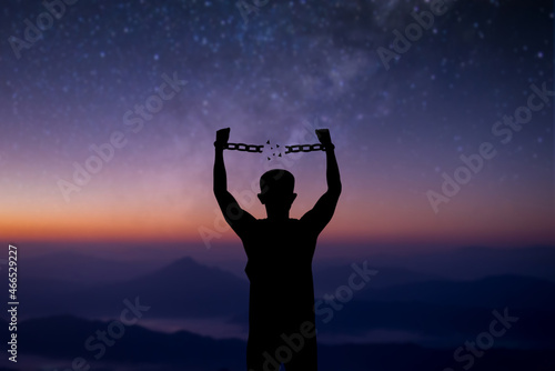 Young man standing alone on top of the mountain with beautiful night sky, star and Milky Way and open both arms with chains on his arms. He felt free from the shackles tied to his arms.