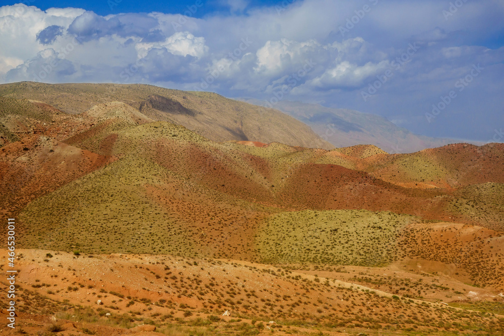 Panorama of unusual multi-colored hills against the backdrop of mountains and picturesque sky. Shot in Surkhandarya region in Uzbekistan near the mountains of the Gissar ridge