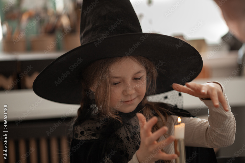 A girl in a witch hat conjures a candle, a child is dressed in a costume for a halloween party, beautiful decor A girl in a witch hat conjures a candle, a child is dressed in a costume for a halloween party, beautiful decor