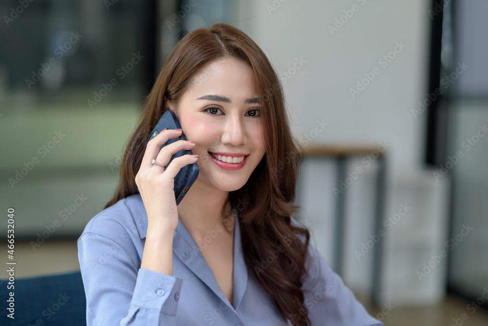 Smiling young Asian woman talking on phone. Beautiful Asia businesswoman spend time in pleasant phone conversation and looking at camera. Smiling young Asian woman talking on phone. Beautiful Asia businesswoman spend time in pleasant phone conversation and looking at camera.