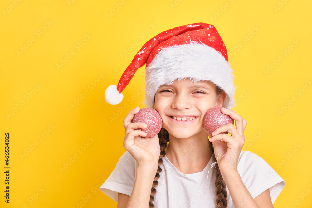 teenage girl in santa claus hat holding christmas balls on yellow background teenage girl in santa claus hat holding christmas balls on yellow background