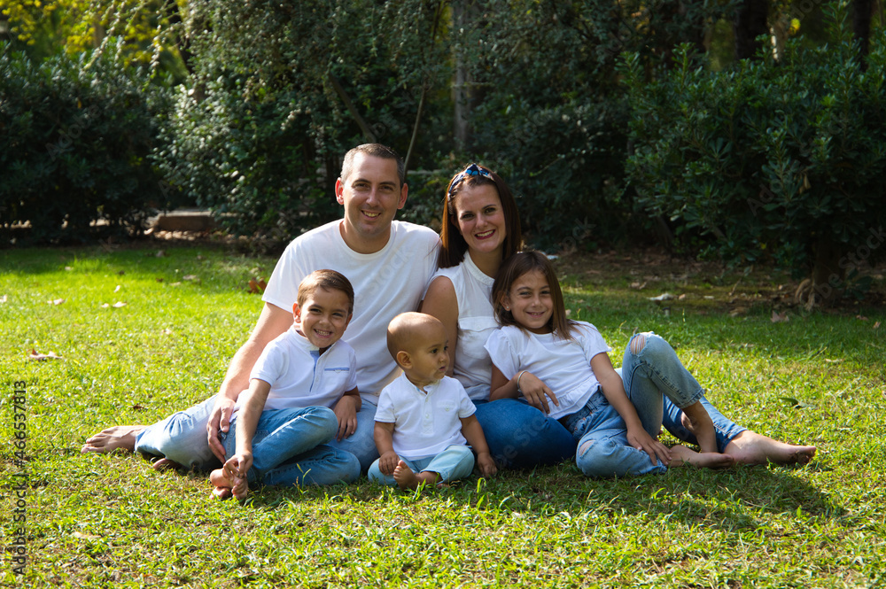 Fototapeta premium Portrait of happy parents with their three children lying in the park. The eldest daughter is a transgender girl. Concept of family happy united family with children.