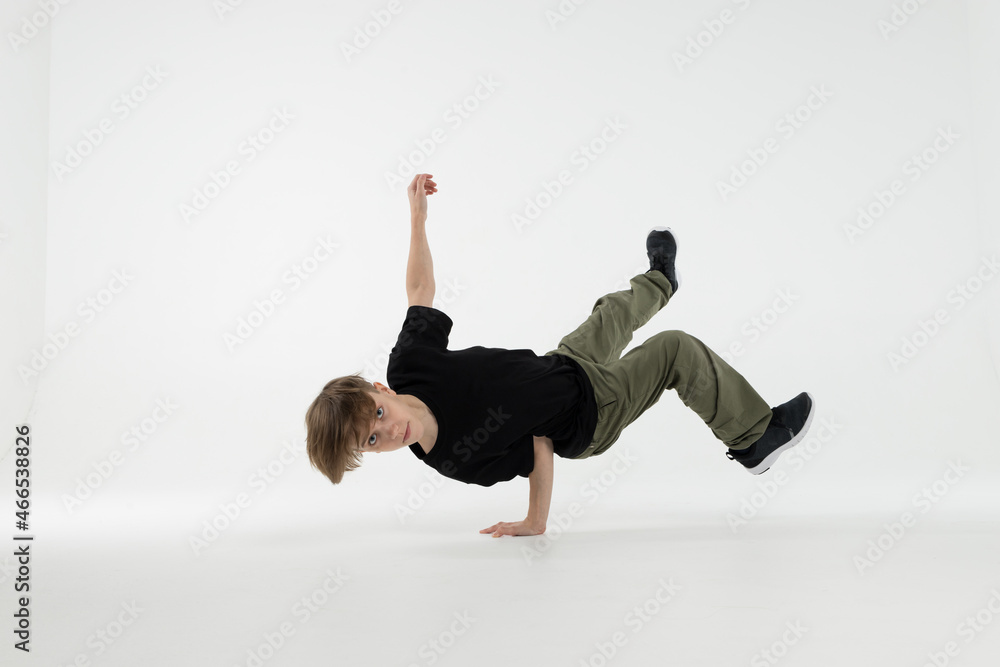 Isolated young Russian teenage boy in black t-shirt hip hop break dancer dancing in studio in white background, performing freeze air chair of downrock breakdance looking into the camera