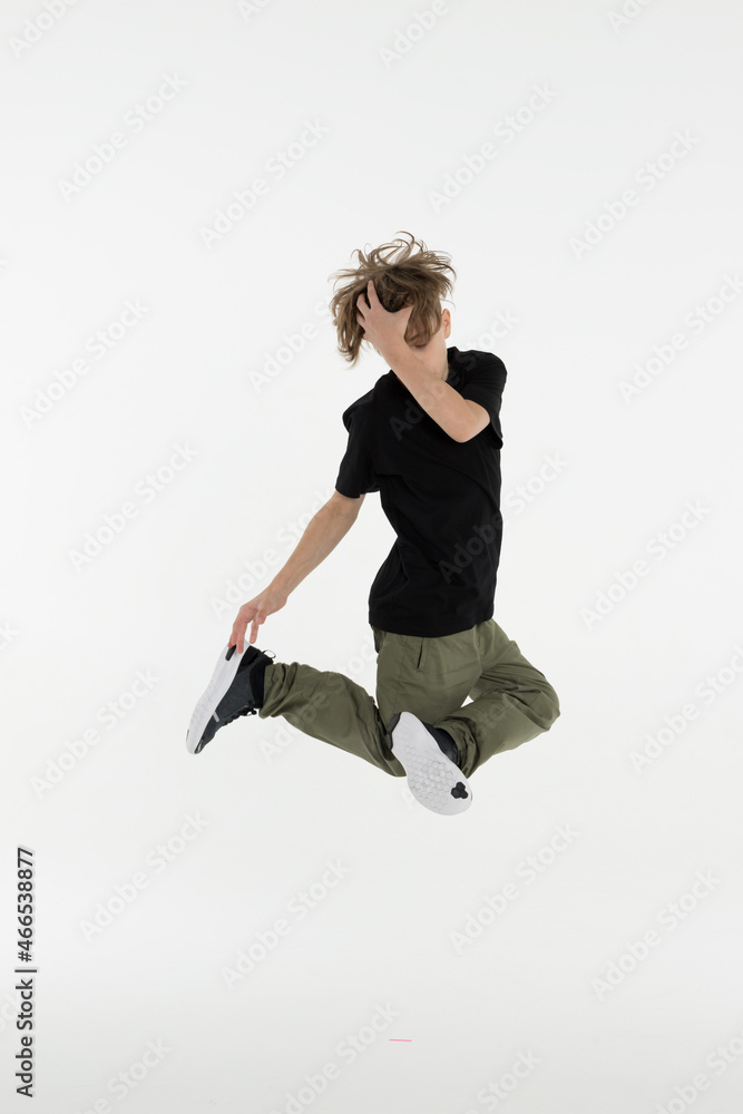 Isolated young Russian teenage boy in black t-shirt hip hop break dancer dancing in studio in white background, jumping and touching his head