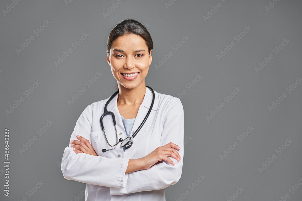 Smiling female doctor with arms crossed isolated against grey background Smiling female doctor with arms crossed isolated against grey background