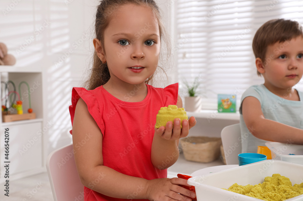 Cute little children playing with bright kinetic sand at table in room Cute little children playing with bright kinetic sand at table in room