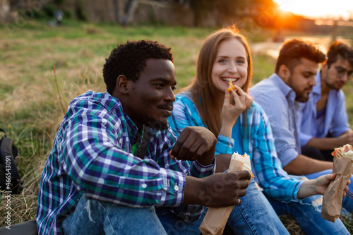 The group of young diverse people eating fastfood on nature