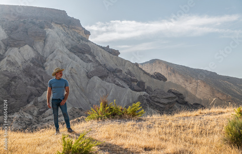 Portrait of adult man in cowboy hat in desert area against mountain and blue sky