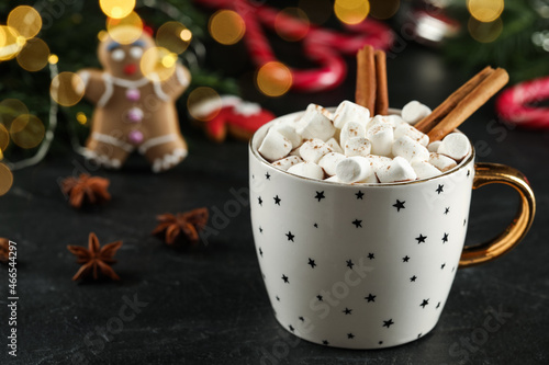 Delicious hot chocolate with marshmallows and cinnamon near Christmas decor on black table, closeup. Space for text