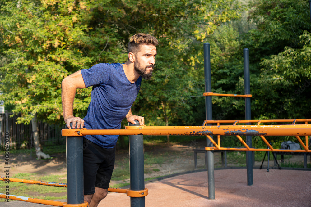 Fototapeta premium Athletic man doing push-ups on the uneven bars.