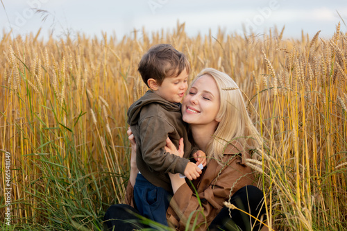 Blonde mother in cloak with a child boy in wheat field