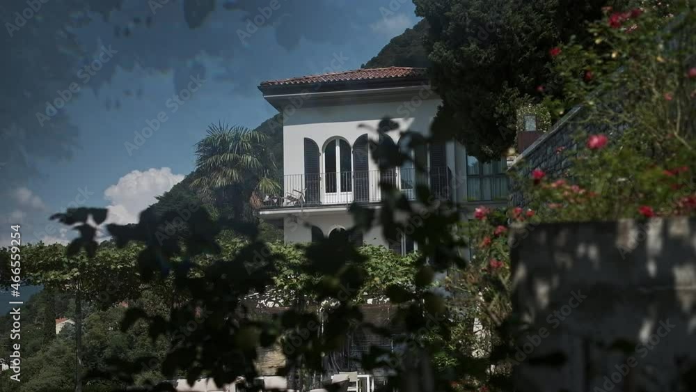 Beautiful House In Rocks Surrounded By Palm Trees And Plants. Wind Shakes Leaves Of Plants. Beautiful House In Rocks Surrounded By Palm Trees And Plants. Wind Shakes Leaves Of Plants.