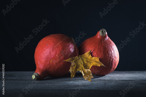 Two pumpkins and a maple leaf on a dark background