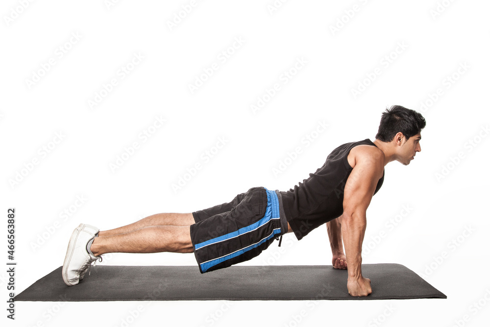 Portrait of strong handsome athletic man standing in plank position, working out on fitness mat, doing Phalakasana exercise on straight arms. Indoor studio shot isolated on white background. Portrait of strong handsome athletic man standing in plank position, working out on fitness mat, doing Phalakasana exercise on straight arms. Indoor studio shot isolated on white background.