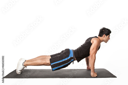 Portrait of strong handsome athletic man standing in plank position, working out on fitness mat, doing Phalakasana exercise on straight arms. Indoor studio shot isolated on white background. photo