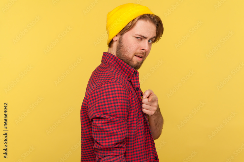 Portrait of guy in beanie hat and checkered shirt pointing finger at camera with flirting expression, choosing you, saying you are what we need. Indoor studio shot isolated on yellow background.