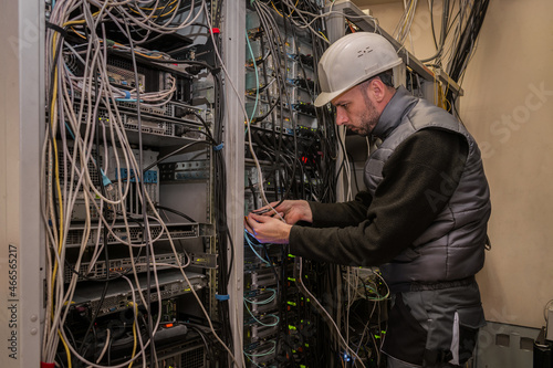 An engineer in a white helmet works in a server room. Technician connects fiber optic cables with network interfaces in the data center