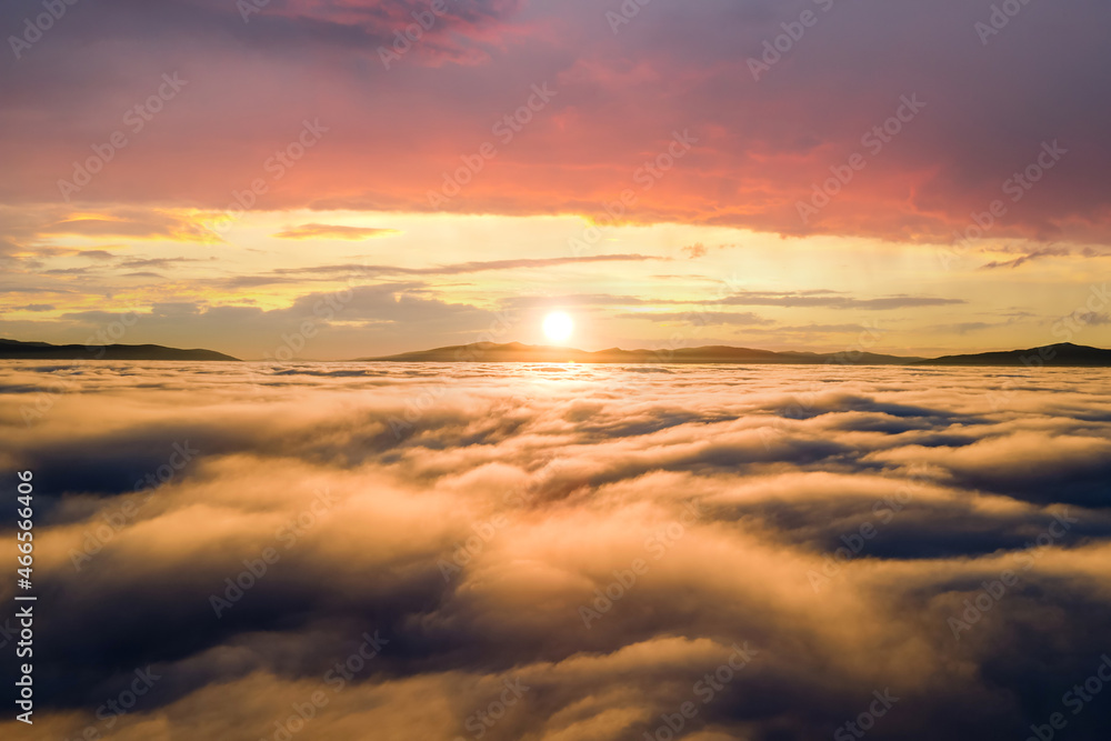 Aerial view of yellow sunset over white puffy clouds with distant mountains on horizon.