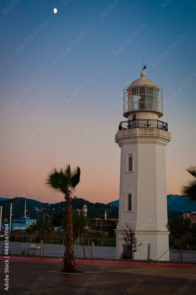 Lighthouse and palm tree on the beach, against the backdrop of mountains. Architectural photography at dusk.