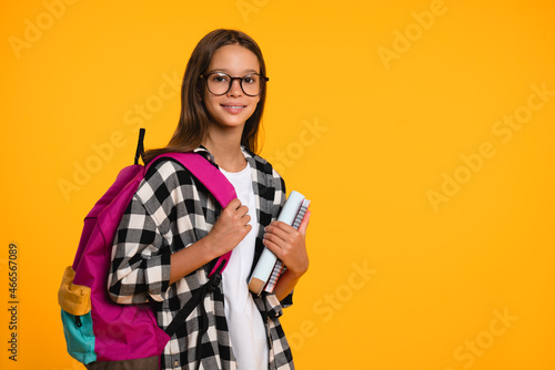 Cropped close up shot of a happy smart caucasian teenager schoolgirl pupil student wearing bag going back to school for new academic educational year isolated in yellow background photo