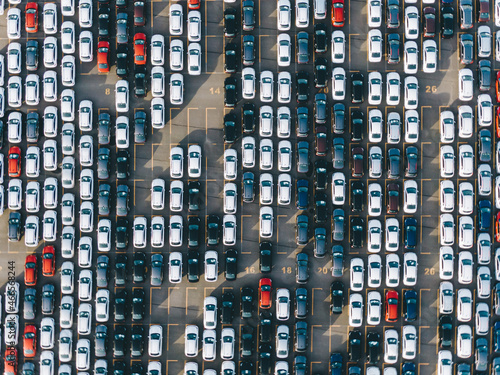 New multi-colored passenger cars stand in straight rows on a giant paved marked parking lot on the territory of an automobile manufacturing plant, overproduction