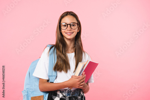 Smiling active excellent best student schoolgirl holding books and copybooks going to school wearing glasses and bag isolated in pink background photo