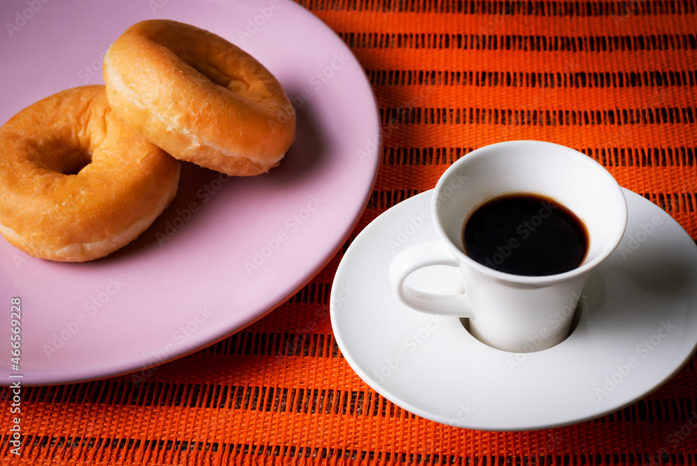 Breakfast or snack of a cup of coffee and some glazed donuts on an orange background. Breakfast or snack of a cup of coffee and some glazed donuts on an orange background.