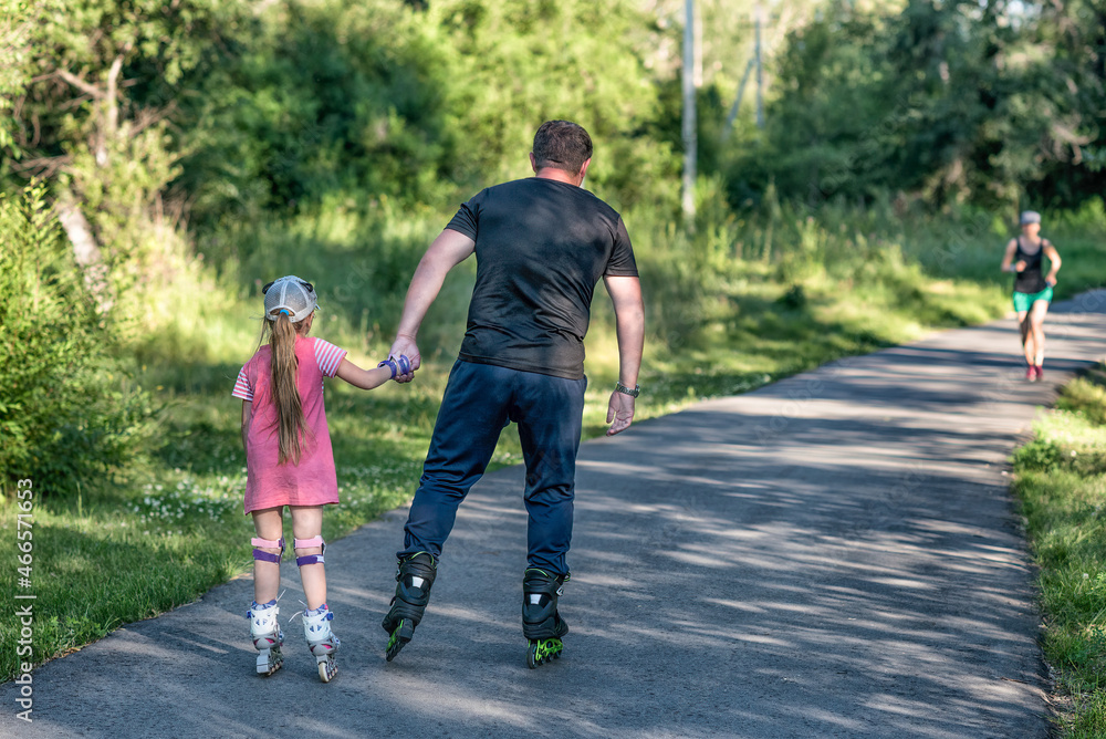A father teaching his daughter roller skating in a park on summer day. Happy week-end. Father's day. A father teaching his daughter roller skating in a park on summer day. Happy week-end. Father's day.