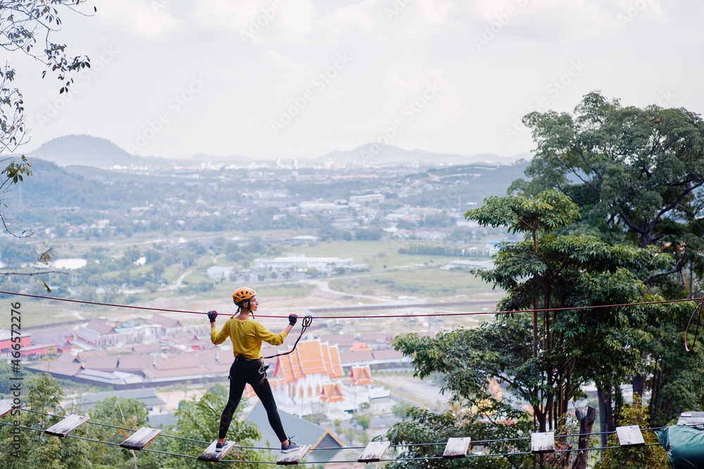 Young woman with climbing gear in an adventure extreme park passing on the high rope road with wonderful view.