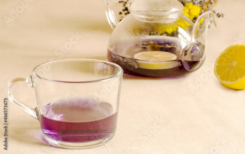 purple tea in a glass mug, a teapot with lemon in the background